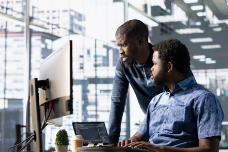 Data engineering IT staff members at PC desk developing machine learning algorithms. African american team in office solving tasks, training large scale deep learning models using computerの写真素材