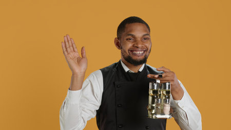 Happy friendly waiter waving hello and welcoming clients at table, holding a cruet set with condiments ready to serve customers. Cheerful lovely staff greeting people at restaurant. Camera A.の写真素材