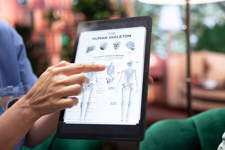 Female osteopath discussing about spinal cord tension diagnosis to elderly people, showing human bones anatomy during home checkup. Nurse offers osteopathy consultation to old patients. Close up.の写真素材