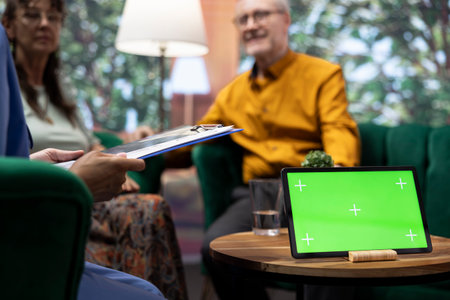 Elderly man and woman talking to nurse at their home with a green screen on tablet, having a fun chat together and asking for guidance. Senior couple feeling good, relaxing at checkup visit.の写真素材