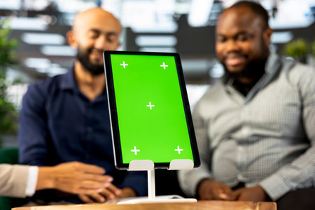 Focus on green screen tablet used by colleagues in blurry background preparing for business meeting. Close up of mockup device used by people doing research analysis for startup organizationの写真素材