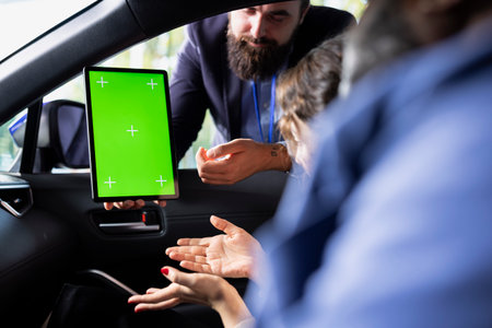 Salesperson using green screen tablet during test drive, negotiating price and car features with...
