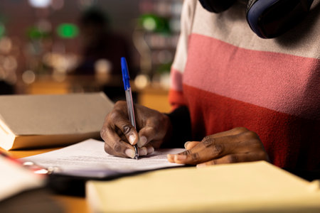 African american college student writes her bachelor degree paper, surrounded by reference books and reliable university study materials. Girl collecting notes and citations for diploma. Close up.の写真素材