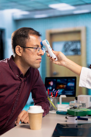 Female specialist consulting a male patient and using thermometer, measuring temperature to offer diagnostics. Indian medic doing fever measurement with a tool, check up visit.の写真素材