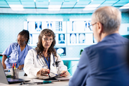 Senior female medic reviewing diagnostics through test results with her patient at medical facility, specialist doing scan interpretation for the correct diagnostic report. Healthcare services.の写真素材