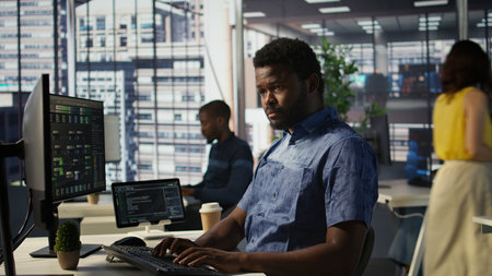 Man checking paperwork details on computer screen, solving tasks. African american bookkeeper in office making sure documents are compliant with quality assurance expectations and standards, camera Bの写真素材