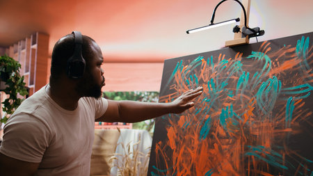 Artist listening to music and creating an abstract painting with his fingers, showing his skills and contemporary ideas in art studio. Creative process finger painting for vibrant artwork. Camera B.の写真素材