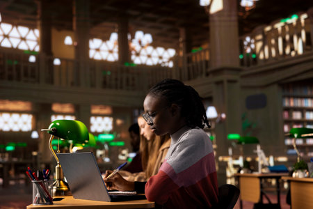 African american student consulting the academic research collection at the library, studying for her upcoming exams to obtain her university diploma. Young adult on a scholarship.の写真素材