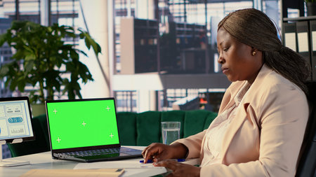 Female leader using green screen on laptop and reviewing finances for her startup, conducting a planning session to develop a new strategy. African american CEO shows leadership skills. Camera A.の写真素材