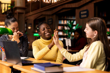 Satisfied teenagers students doing high five next to tutor in the library, feeling happy with their progress on school subjects. Professor being proud of her scholars at private lessons.の写真素材