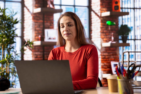 Focused woman engaged in online research for a work project at home office, sitting at the laptop and reading articles on the internet. Person surfing webpages and gathering data, telework.の写真素材