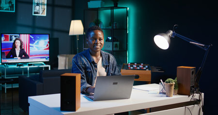 Portrait of smiling african american woman at desk typing on laptop keyboard, solving tasks. Joyful remote worker using notebook to send emails to business partners from living room, camera Bの写真素材