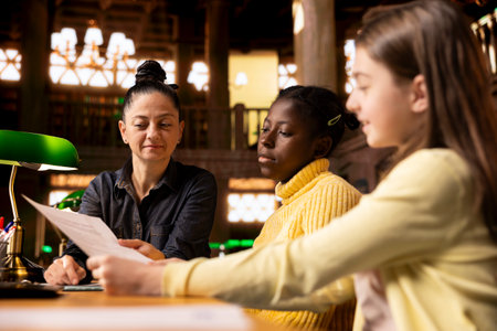 Female tutor helping her teen pupils prepare for an exam by providing materials for learning,...