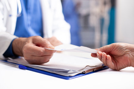 Closeup of white person in lab coat giving prescription paper to patient after medical exams. Selective focus of caucasian people holding medical document on table with clipboard nearby.の写真素材