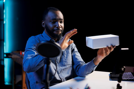 Smiling content creator at home holding product box in hand, preparing to unbox in after finishing video introduction. Trending influencer doing tech item review for viewersの写真素材