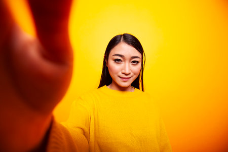 Smiling asian female individual holding the camera, making a video for her online audience....