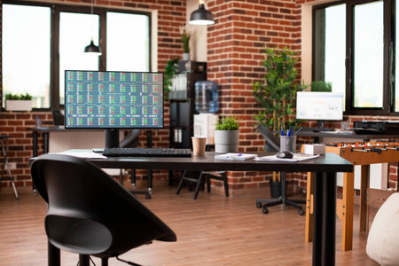Spacious startup office with no people highlights a desktop monitor presenting company trading data results. Organized supplies and plant decorations enhancing professional workspace.の写真素材