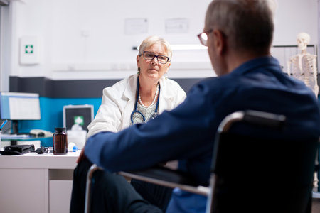 Retired male patient in wheelchair provides health updates to his senior female physician at clinic....