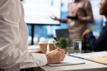 Female investor takes notes during financial projection in a meeting, trying to obtain funds to...