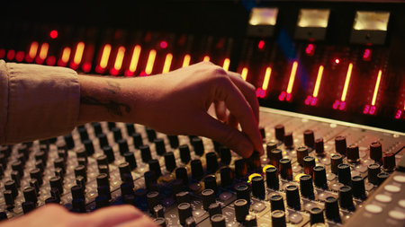 Audio technician twisting pre amp knobs and buttons on panel board in control room, using editing...