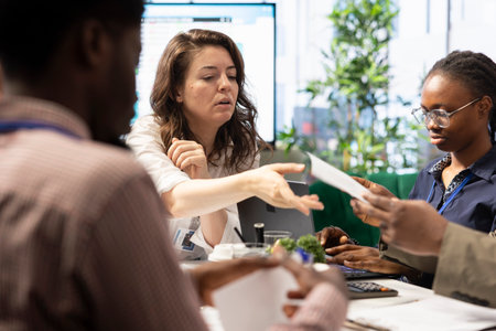 Diverse team of business people meeting in boardroom to examine annual records, looking over sales...