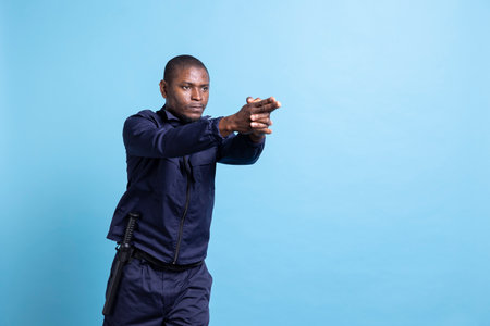 African american security officer mimicking an armed attack on camera, holding an imaginary weapon. Protection agent pretending to have a gun in his hands, combat demonstration in studio.の写真素材