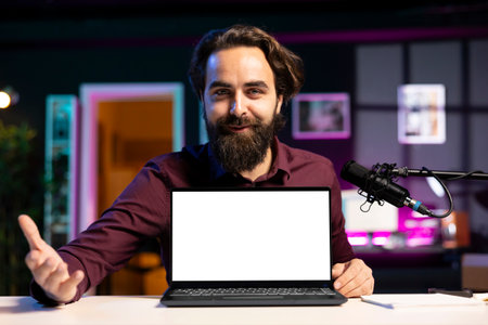 Portrait of cheerful man in studio filming tech tutorial on how to do maintenance on mockup laptop. Happy online show host teaching subscribers how to open and fix isolated screen notebookの写真素材