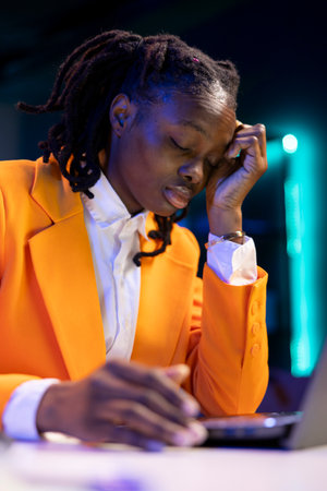 Fatigued gen Z teleworker feeling overworked, closing eyes after working too much on job tasks. Exhausted young woman trying to relax and regain energy while working from homeの写真素材