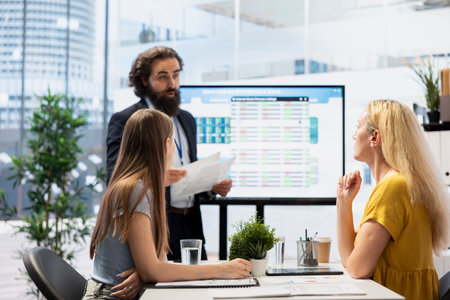 Team leader in company financial department showing stock portfolio on big screen containing...