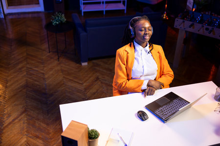 Ecstatic gen Z woman in RGB lit apartment listening music during relaxation time, feeling engrossed. Overjoyed young girl having fun in living room hearing thrilling songs through headphonesの写真素材