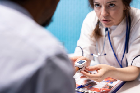Physician measuring the oxygen saturation and pulse rate using an oximeter during check up visit, consulting her patient with modern medical equipment. Vital signs measurement. Close up.の写真素材