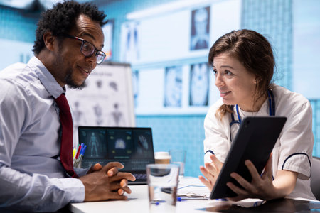 Doctor and patient engage in a discussion about diagnostic results, providing professional healthcare advice during medical examination in cabinet. Showing the medical results on tablet.の写真素材