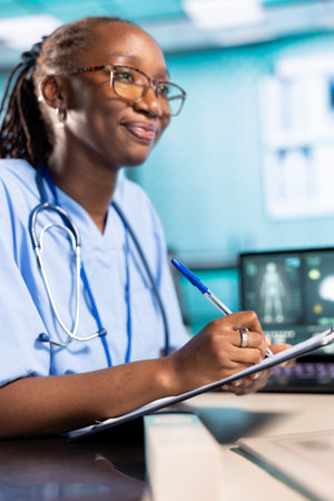 African american medical assistant takes notes on hospital records files during checkup and discussion with old people. Female nurse collecting information and symptoms to ensure a recovery plan.の写真素材