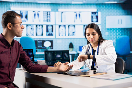 Doctor measuring patient pulse with a smartwatch during a medical visit. Healthcare provider uses modern technology for heart rate and blood pressure diagnostics in a professional office.の写真素材