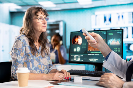 Aged physician uses a digital thermometer to check for fever and other flu symptoms, professional tools for accurate diagnostics. Instruments for wellness.の写真素材