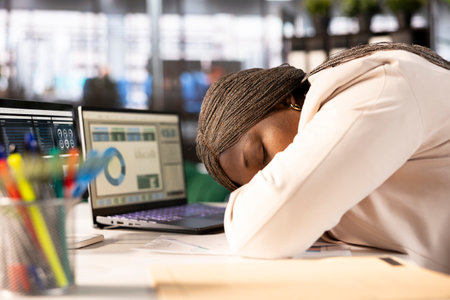 Overworked woman falling asleep at desk while looking over statistics charts on laptop, researching data. Tired worker napping in office on notebook while doing research for marketing projectの写真素材