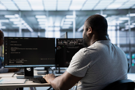 African american admin programming in server room housing advanced equipment storing massive datasets. Engineer typing code on PC to mend data center racks doing complex computational operationsの写真素材