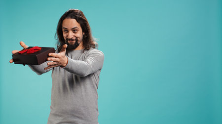 Portrait of smiling man offering gift for birthday celebration, isolated over studio background. Cheerful person giving present during celebration party, studio backdrop, camera Bの写真素材