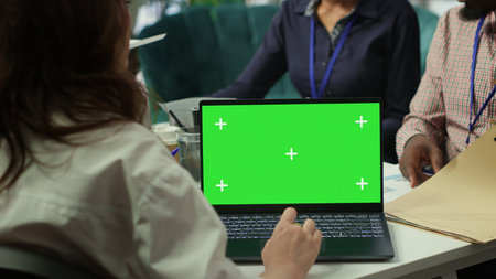 Diverse team of business associates looking at mockup chroma key screen during executive board meeting, utilizing smart technology. Enterprise staff develop effective business strategies. Camera A.の写真素材