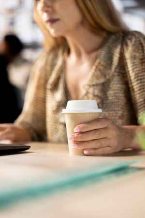 Account executive multitasking on her computer and drinking coffee, early morning start to finish business tasks and operations. Woman reviewing financial documents for company success. Close up.の写真素材