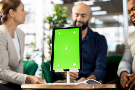 Focus on isolated screen tablet in front of businesspeople talking in startup company, looking at financial business documents. Close up of mockup device used by office clerks in blurry backgroundの写真素材