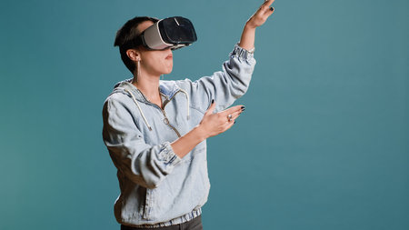 Groovy edgy woman wearing a 3d virtual reality headset in studio, using artificial intelligence and glasses against blue background. Modern funky girl with style uses a modern gadget.の写真素材