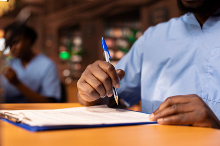 African american student takes notes about medical practice to prepare for an exam, studying to obtain his med school diploma and build a career in healthcare. Scholar writes data. Close up.の写真素材