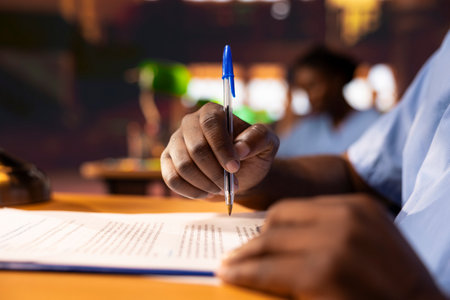 Black male pupil makes notations about practice methods to prepare for an exam, studying at the library to obtain his med school diploma for a medical career. Student does a summary. Close up.の写真素材