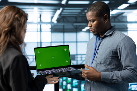 Team of engineers working in server farm, using green screen laptop to analyze data. Employees...