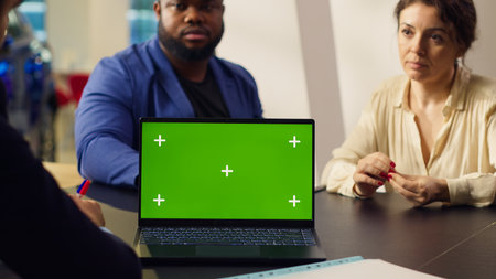 Customers in showroom looking for new vehicle to purchase, being shown options by salesman on mockup laptop. Agent using green screen notebook to help clients evaluate cars, camera Aの写真素材