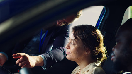 Showroom salesman showing purchasable extra car features on tablet to clients after they finished test drive. Dealership agent showing vehicle addons catalog to husband and wife on device, camera Aの写真素材