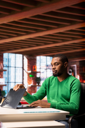 Remote employee closing laptop in home office after finishing writing emails. African american teleworker ending work shift, closing notebook after being done with projectの写真素材