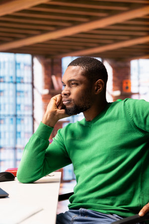Man having hard time coming up with ideas for work project at home office desk. Stumped african american remote employee ruminating in apartment workspace, thinking how to solve tasksの写真素材