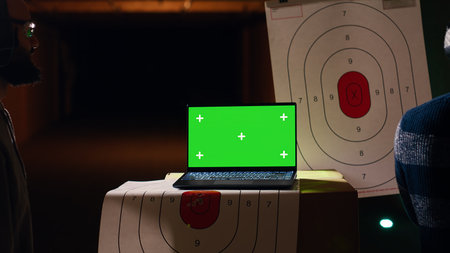 Green screen laptop next to shooting gallery safety officer watching client shoot at targets, supervising him. Mockup notebook and firing range expert teaching man how to use firearms, camera Bの写真素材